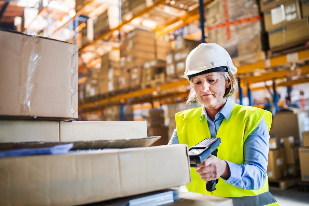 Senior warehouse woman worker using a mobile handheld PC with barcode scanner.