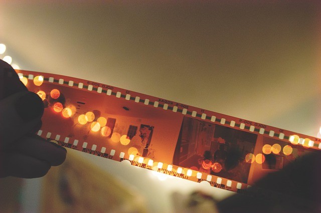 Close-up of a hand holding a film negative in front of a white laptop screen, ready to be scanned using the Helmut app.